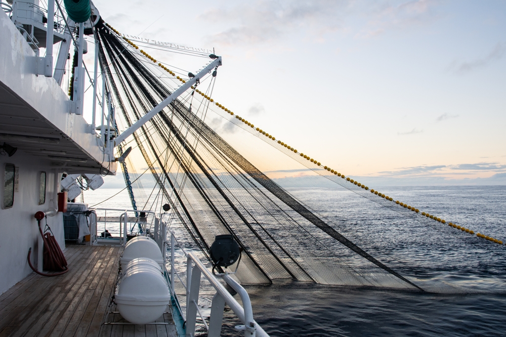 A commercial fishing boat that have thrown a net to the sea to do fishing at sunset